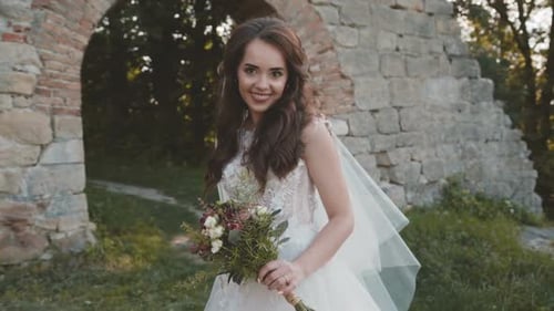 Happy Bride with Bouquet in Hands Smiles and Poses at Ancient Castle