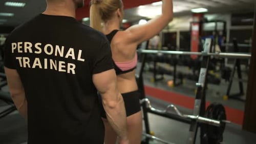 Young Female Doing Weight Bar Lifting Exercise Under Control of Her Trainer