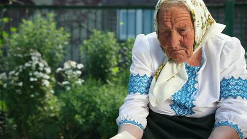 An Old Grandmother is Sitting on the Street and Reading a Book