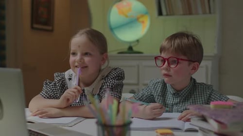 Two Kids Distant Learning at Home Listening to Online Teacher at Laptop Sitting at Desk with