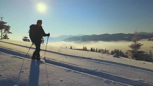 Hiker with Backpack Walking on Snowy Mountain Hillside on Cold Winter Day