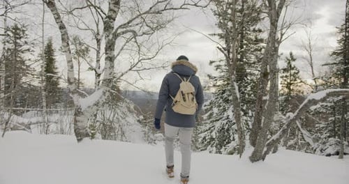 Back View of Young Man Tourist Walking in Snowy Forest on Winter Day