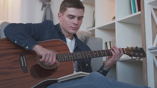 Young Man Composes Music at Home with Guitar