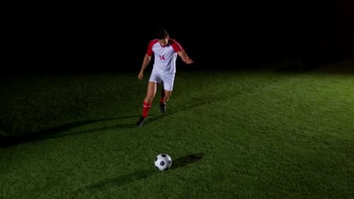 Soccer Player Kicks Ball on Green Field at Night