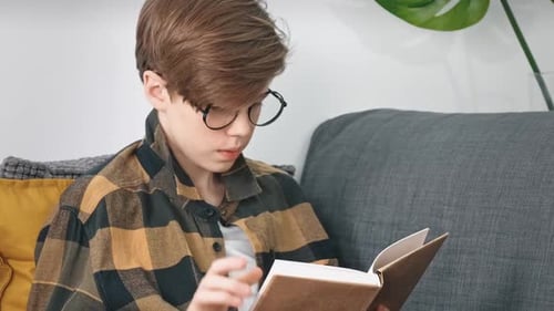 Ein Teenager mit Brille liest begeistert ein Buch, während er zu Hause auf der Couch sitzt