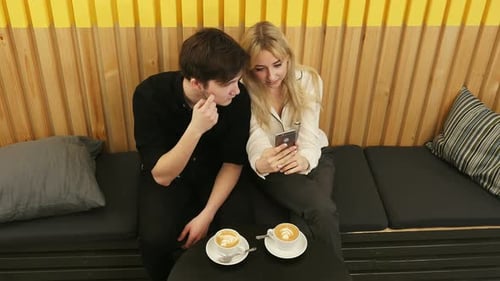 Happy Couple Using Smartphone Together and Drinking Coffee in Cafe