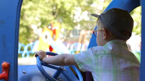 A little boy is played on the playground in a toy car.