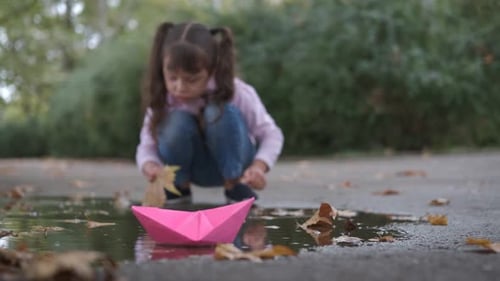 Girl Plays With Paper Boat in Autumn Puddle