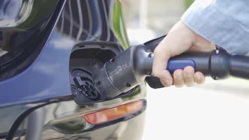Hand plugging in EV car charger or electric vehicle. Cable connect to gas station