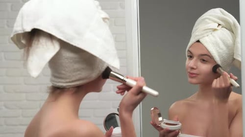 Young Woman Applies Makeup with Brush in Bathroom