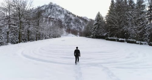 Forward Aerial Over Man Walking with Snowshoes on Mountain Snow Covered Field Near Pine Forest Woods