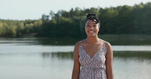 Beautiful Smiling Cheerful Woman in Floral Dress is Hanging Out at the Lake Her Hair is Tied Up in a