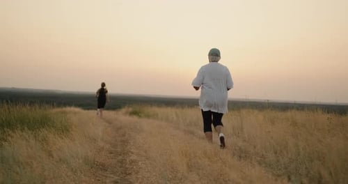 Senior and Adult Running on Grassy Trail at Sunset