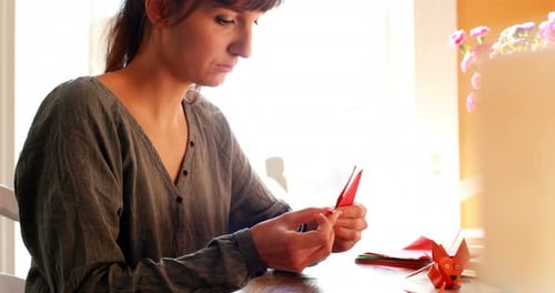 Woman Folds Origami Paper at Table Indoors