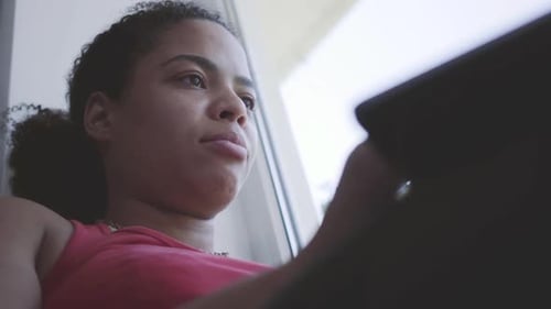 Cute Young African American Woman Sitting on the Window Sill Typing on Her Laptop