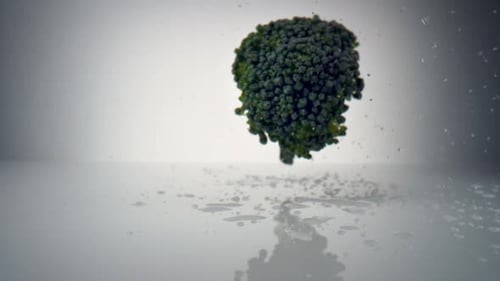 Fresh Broccoli Falling onto White Reflective Surface
