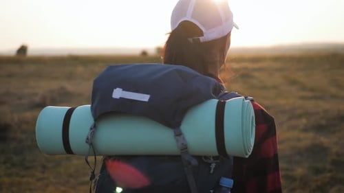 Hiker with Backpack Walking Across Rural Field at Sunrise