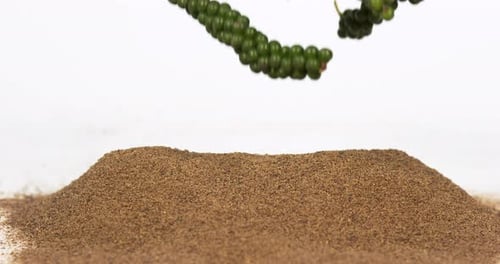 Green Peppercorns Falling onto Pile of Ground Pepper