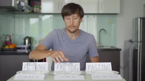 Un jeune homme est assis près de la table avec des assiettes vides et des signes de jeûne. Il met des lunettes avec de l'eau