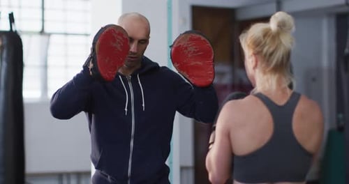Caucasian female boxer wearing boxing gloves training her punches with male trainer at the gym