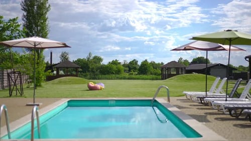 Wide Shot Blaues Schwimmbad mit grüner Wiese und weißen Wolken am Himmel im Hintergrund