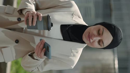 Woman Holding a Coffee Cup Looks at Phone