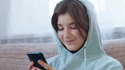Girl Using Mobile Phone Indoors Wearing Hooded Sweatshirt