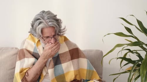 Senior Man Coughing on a Couch Under Blanket