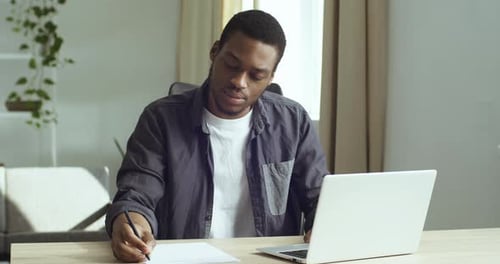 Man Working at Laptop Writing on Paper at Desk