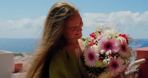 Tanned Young Woman Touches and Sniffs Flowers in Sunlight