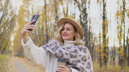 Beautiful Blonde Woman in a Brown Hat Takes a Selfie in the Autumn Park