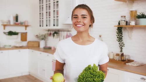 Smiling Woman Eats Apple and Holds Lettuce