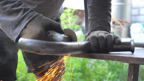 Close Up Hands of Mechanic Holding Instrument and Grinding Metal on His Workplace