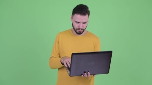 Bearded Man Uses Laptop Against Green Background