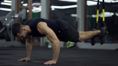 Sportif faisant des exercices abdominaux au sol avec des sangles TRX au gymnase