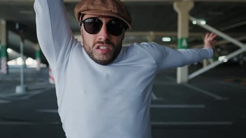 Young Man with Beard Actively Dancing While Walking Down the Street on Sunset Background. Urban