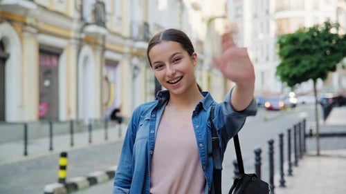 Young Woman Waving Hello on City Street