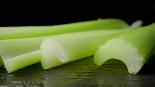 Row of Green Celery Stalks Lying on Black Board on Isolated Black Studio Background