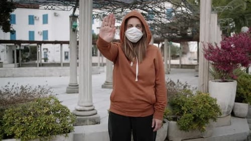 Woman in orange sweater and medical mask stay on empty street. Coronavirus pandemic concept.