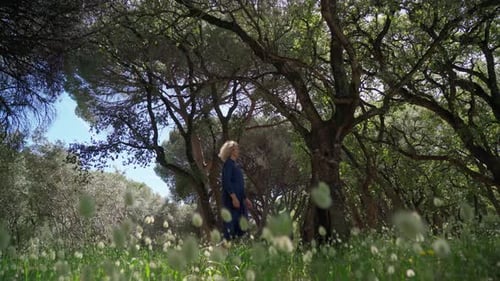 A European Woman Middleaged in a Dress Walks on a Prak with Tall Grass