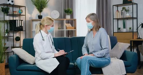 Medical Worker in Facial Mask and White Gawn Visiting Female Patient at Home During Desease