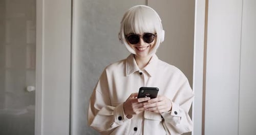 Smiling Woman with Headphones Using Smartphone Indoors