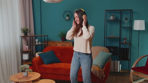 Overjoyed Young Woman in Wireless Headphones Dancing Singing on Cozy Couch in Living Room at Home