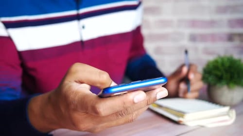 Nahaufnahme eines jungen Mannes mit Smartphone und Schreiben auf Notizblock
