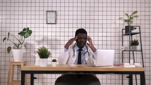 Worried Doctor Massaging Temples at Desk