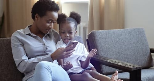 Mother and Daughter Using Smartphone on Couch Indoors