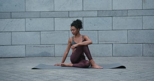 Une femme afro-américaine fait Fish Lord Asana assise sur un tapis