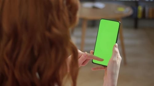 Back View of Redhead Woman Holding Chroma Key Green Screen Smartphone Watching Content With Touching