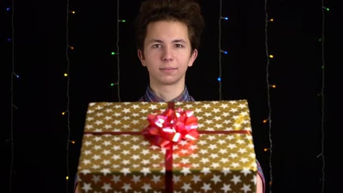 Young Adult Holds Christmas Gift in Front of Lights