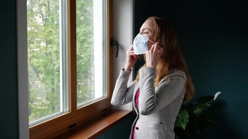 Woman Puts on Face Mask by Window